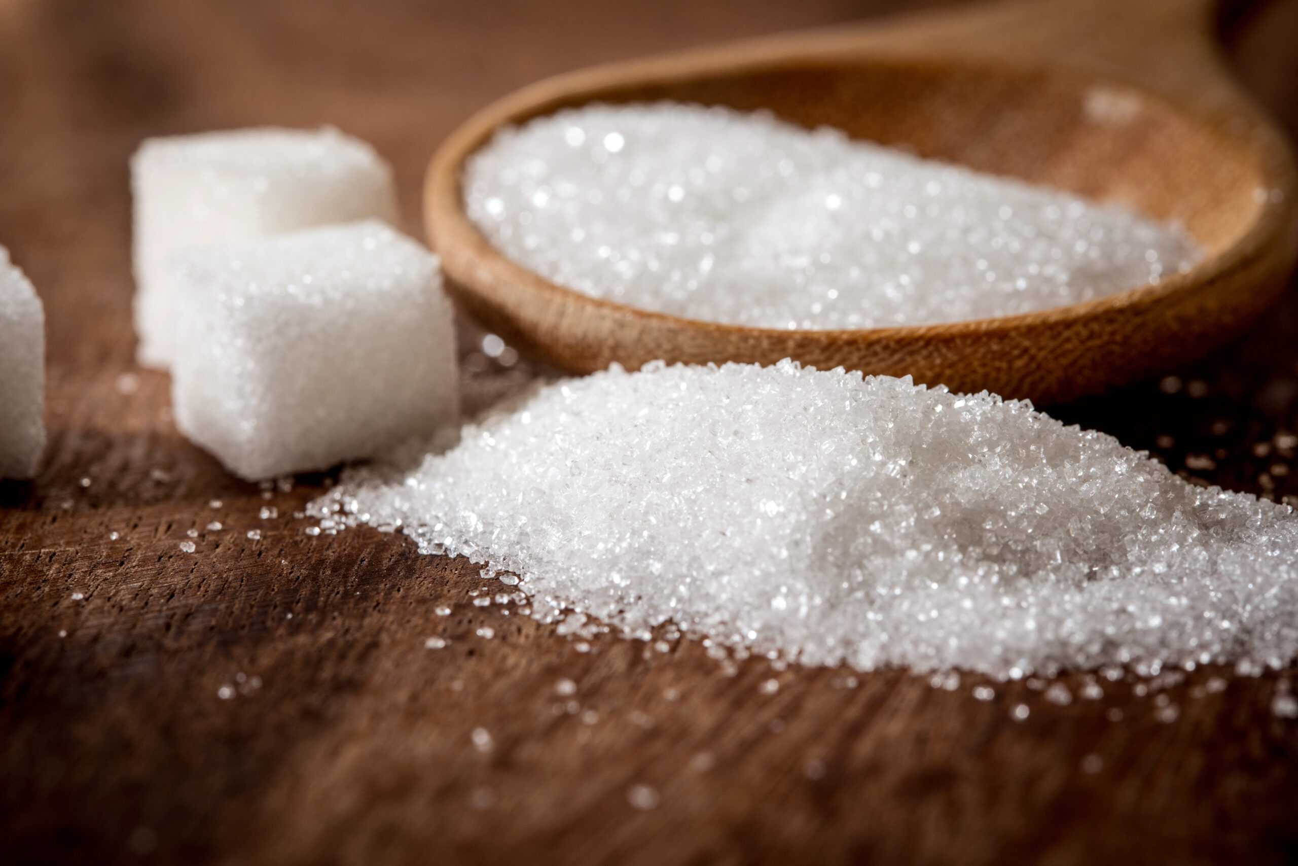 Close up sugar cubes and cane in wooden spoon on the table